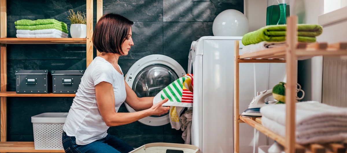 Une femme sort le linge du lave-linge qui attend d'être séché au sèche-linge