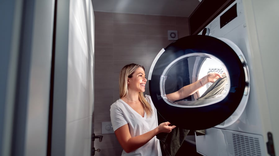 Une femme blonde sèche du linge dans un sèche-linge de grande capacité de poids de linge